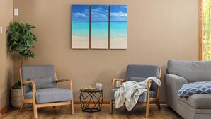 A living room with a beige wall, a large window, a blue sofa, two armchairs, a small round table with a bowl and cup, and a potted plant. - Total Seclusion! Hot tub,  Traverse City downtown 10 min, Booking for summer!  (Traverse City)