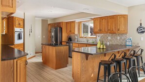 A spacious kitchen with wooden cabinets, a central island, and bar stools. - Total Seclusion! Hot tub,  Traverse City downtown 10 min, Booking for summer!  (Traverse City)