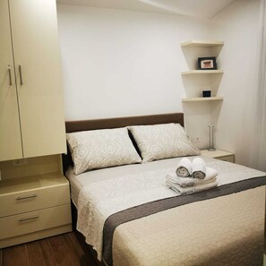 Una camera da letto ordinata con un letto, cuscini, un comodino, una lampada e un armadio.