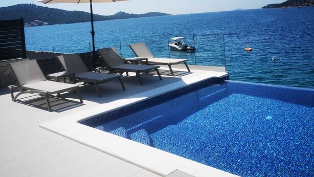 A pool area with lounge chairs and an umbrella, overlooking a body of water with boats and hills in the background. - Villa Marijo with sea view and pool, Croatia (Razanj)