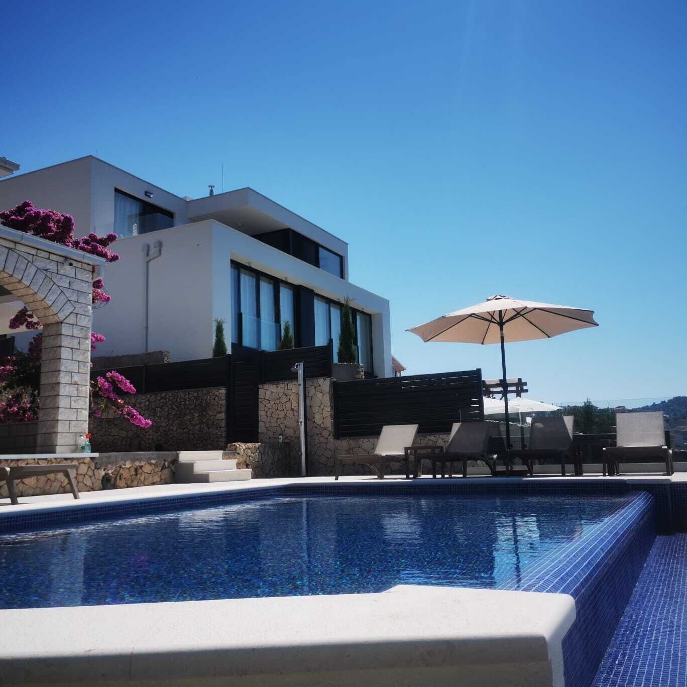 A modern pool area with a clear blue pool, lounge chairs, and an umbrella.