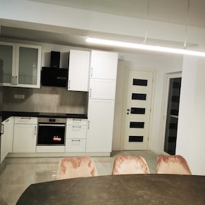 Una cucina compatta con mobili bianchi, una cappa aspirante nera e un forno integrato. Sulla parte anteriore, due sedie e un tavolo.