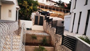 A narrow, stone-walled pathway with steps leading to a gated entrance, flanked by modern buildings and a white fence. - Villa Marijo with sea view and pool, Croatia (Razanj)
