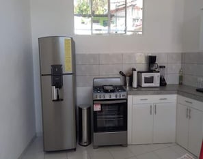Une cuisine compacte équipée d’un réfrigérateur en acier inoxydable, d’une cuisinière à gaz, d’un four à micro-ondes et de meubles de rangement blancs.
