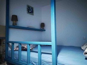 A room with a bunk bed, a desk with a lamp, and a small shelf with a picture.