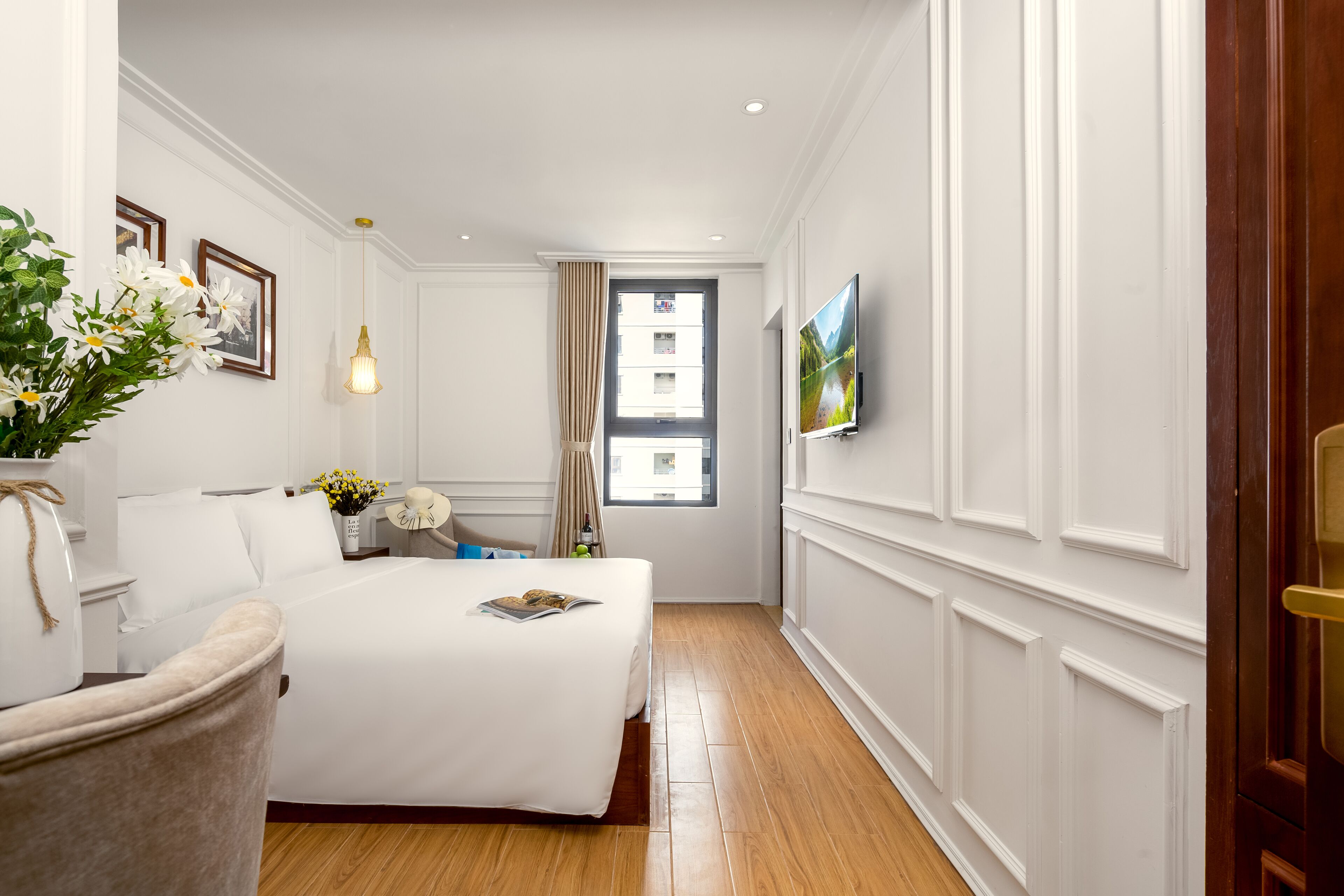 Une chambre d’hôtel avec un lit, une chaise, un vase de fleurs, un tableau au mur et une fenêtre.
