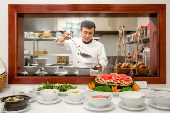A chef serving food behind a counter with various dishes and a decorative watermelon centerpiece. - Menora Grand Da Nang (Da Nang)