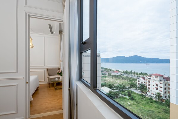 A hotel room with a large window, a bed, a sofa, and a small table with a vase of flowers. - Menora Grand Da Nang (Da Nang)