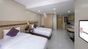 A hotel room with two beds, a small table with a vase, a desk, and a kitchenette. - Cebu Family Suites powered by Cocotel (Cebu City)