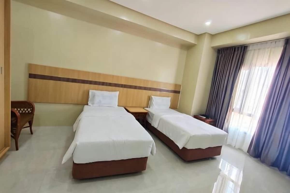 Une chambre d’hôtel avec deux lits, une tête de lit en bois, une table de chevet et une fenêtre avec des rideaux.