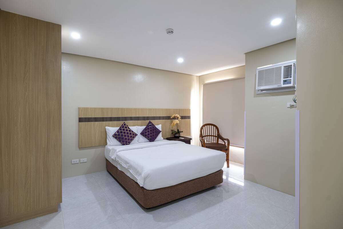 Une chambre à coucher avec un lit, une tête de lit en bois, du linge de lit blanc et une petite table de chevet avec une lampe.