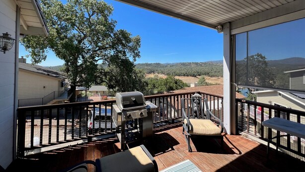 Une terrasse extérieure couverte, équipée d’un barbecue, de sièges et offrant une vue sur un arbre et des collines lointaines.