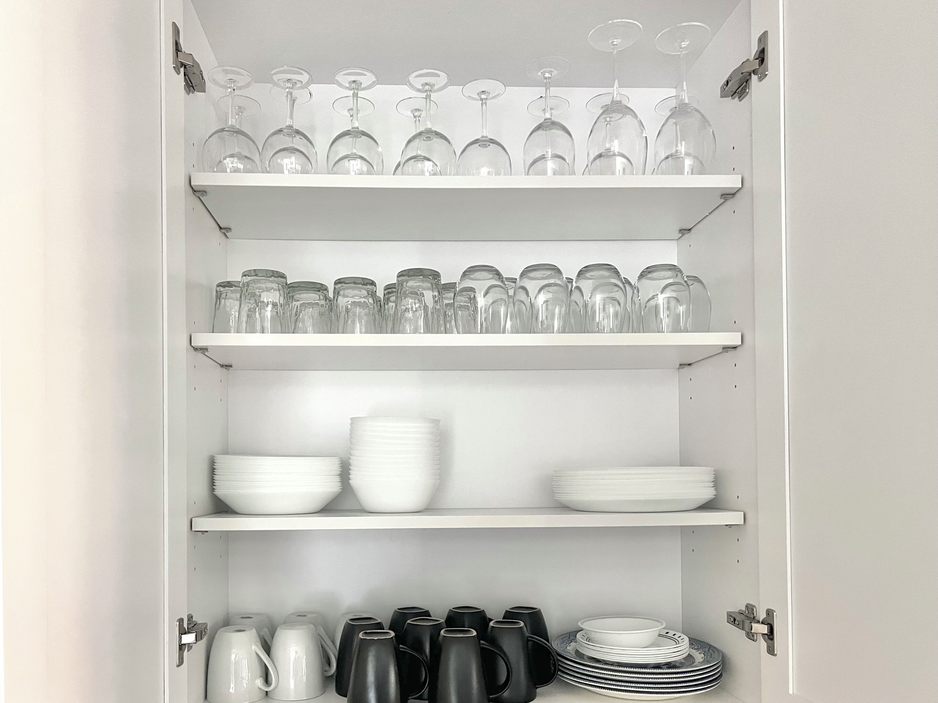 A cabinet with shelves holding wine glasses, glassware, plates, and mugs.