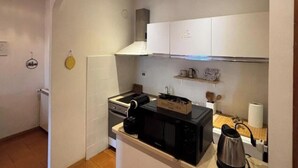 Une cuisine de taille réduite, équipée d’une cuisinière, d’un four à micro-ondes, d’une bouilloire et de meubles de rangement blancs.