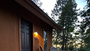 En træterrasse med to Adirondack-stole og et lille bord, der fører hen til en mørk dør med en lampe over.