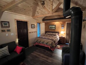 A cozy room with a bed, a wooden ceiling, a fireplace, a couch, and a door. - Rustic guest cabin set in the high country between Telluride and Ridgway (Placerville)