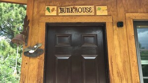 En træfacade med en mørkebrun dør, et skilt der siger "BUNKHOUSE", og en fuglekasse med en fugl på den.