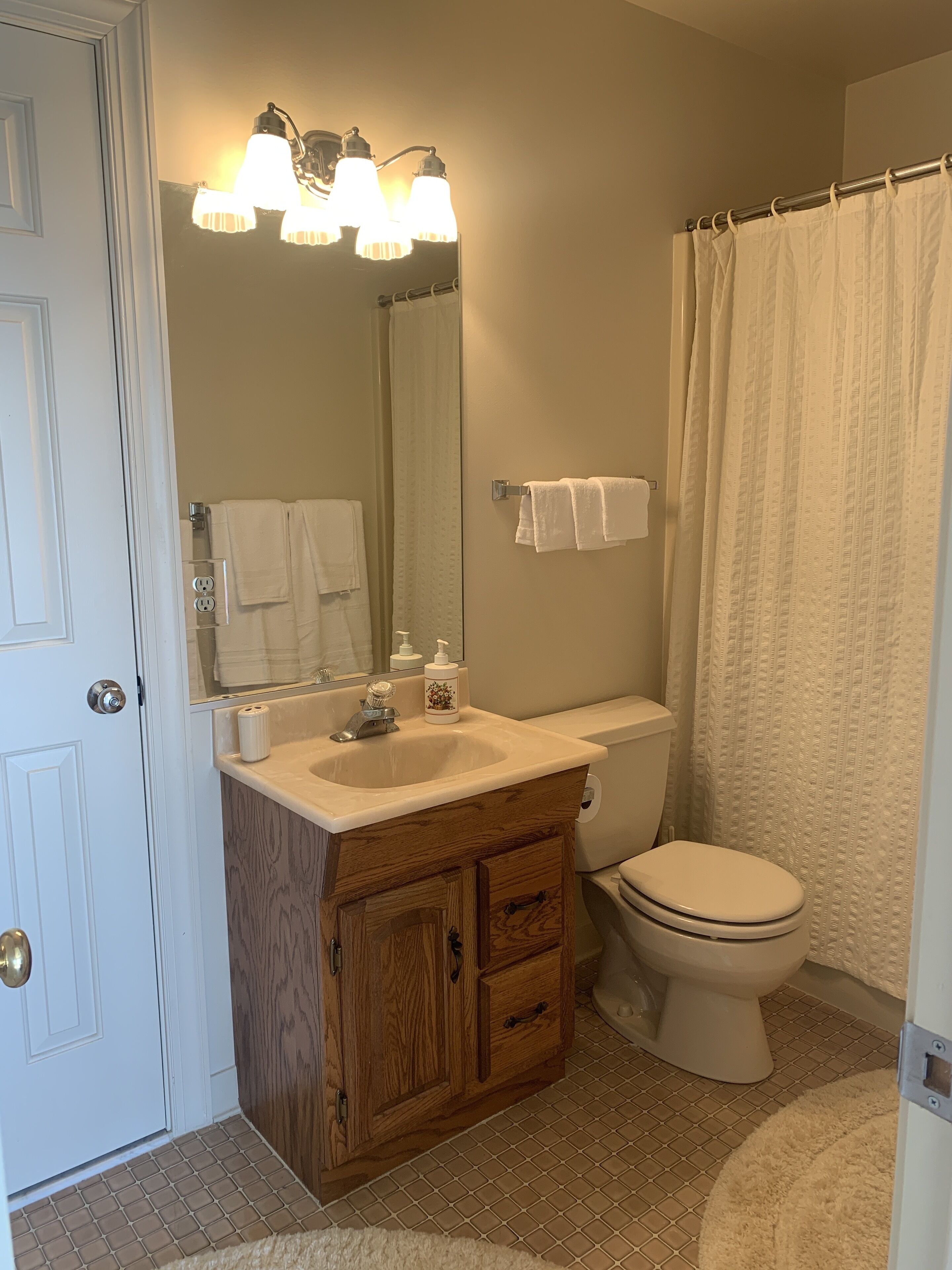 A bathroom with a wooden vanity, a sink, a toilet, a mirror, and a shower curtain.
