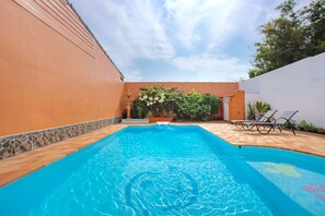 A swimming pool with clear blue water, surrounded by a tiled deck, a white wall, and a brick wall with a small garden. - Holiday Bliss 3BR Pool Villa Lancelot 2 (Rawai)