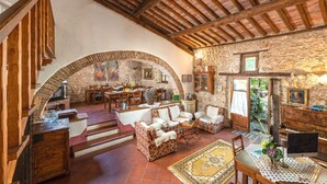 A rustic interior with a stone archway leading to a dining area, wooden furniture, and a traditional fireplace.