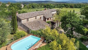 A villa with a swimming pool surrounded by lush greenery and a view of distant hills.