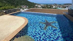 A rooftop pool with a starfish mosaic, surrounded by a stone wall and a view of a coastal town. - Sea view apartment, 5 min drive from Kata Beach (Karon)