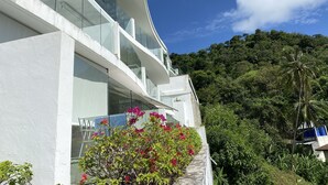 A modern building with a curved facade, large windows, and a balcony overlooking lush greenery and a clear sky. - Sea view apartment, 5 min drive from Kata Beach (Karon)