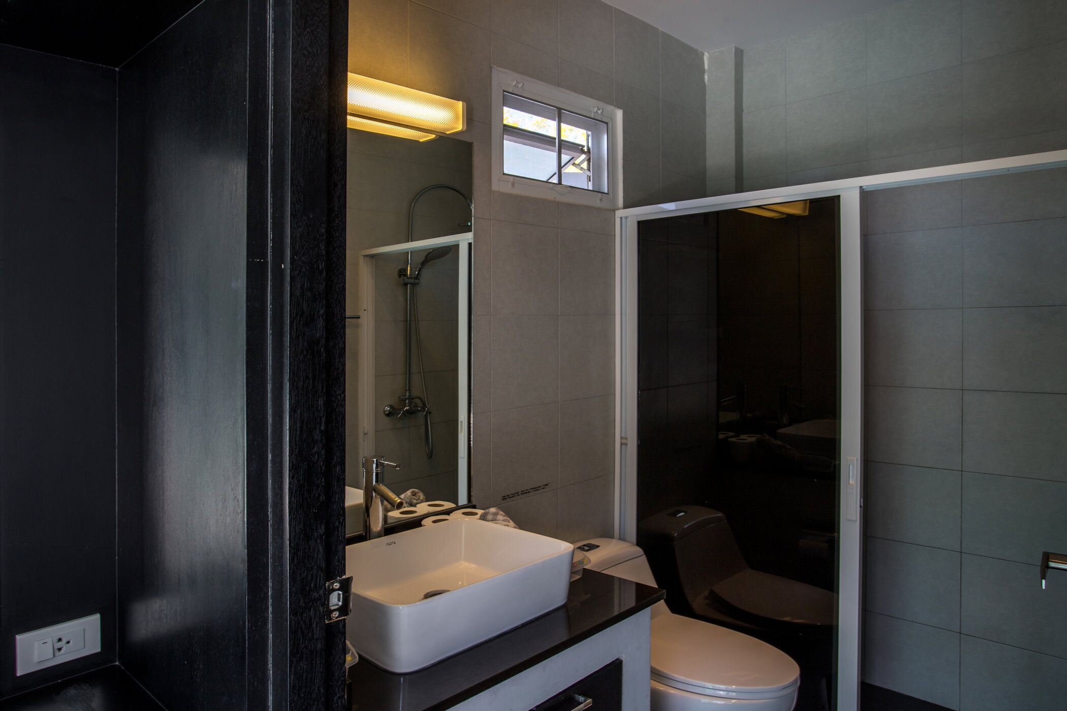 A modern bathroom with a black vanity, white sink, and a toilet.