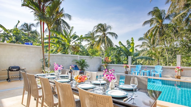A poolside dining area with wicker chairs, a table set for six, and a view of the pool. - Tropical Vibe 5BR Pool Villa Nikkie 3 (Rawai)