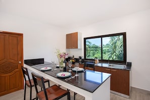 A modern kitchen with a large island, wooden cabinets, and a view of greenery through the window. - Tropical Vibe 5BR Pool Villa Nikkie 3 (Rawai)