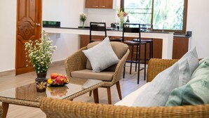 A living room with wicker furniture, a glass coffee table, and a view of a kitchen and dining area. - Tropical Vibe 5BR Pool Villa Nikkie 3 (Rawai)
