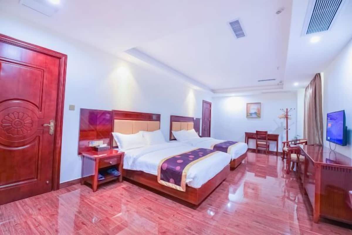 A hotel room with two beds, a desk, a chair, a TV, and a wardrobe.
