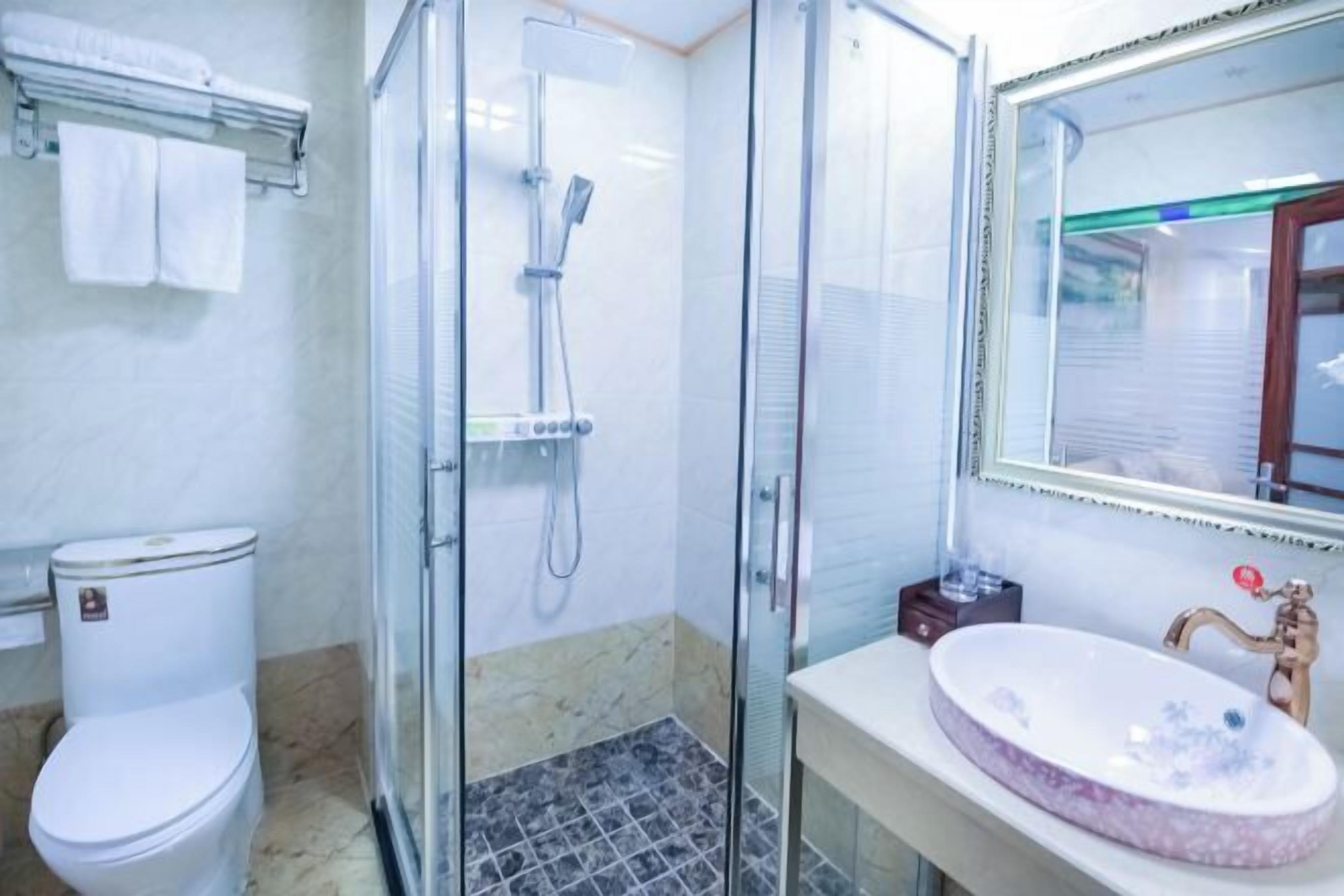 Un bagno con doccia vetrata, un water, un lavandino con lavabo in marmo e uno specchio con cornice in legno.