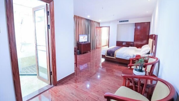 A hotel room with a bed, a TV, a seating area with chairs, and a sliding glass door leading to an outdoor area. - Hao Ye Hotel (Yangjiang)