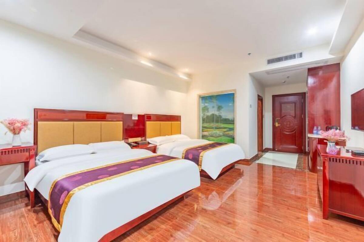 A hotel room with two beds, wooden flooring, a red desk, and a painting on the wall.