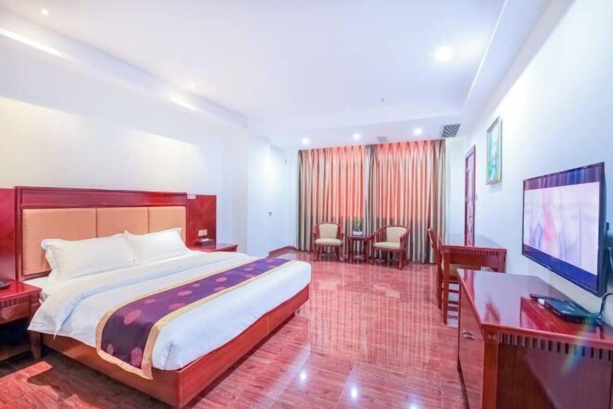 A hotel room with a large bed, a desk with a computer, a TV, and a seating area with chairs.
