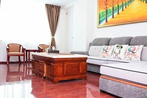 Una sala de estar moderna con una mesa de centro de madera, un sofá gris con almohadones coloridos y un cuadro de un camino bordeado de árboles en la pared.