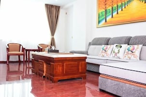 Una sala de estar moderna con una mesa de centro de madera, un sofá gris con almohadones coloridos y un cuadro de un camino bordeado de árboles en la pared.