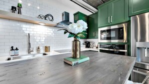 Una cocina moderna con armarios verdes, electrodomésticos de acero inoxidable y encimera de mármol.