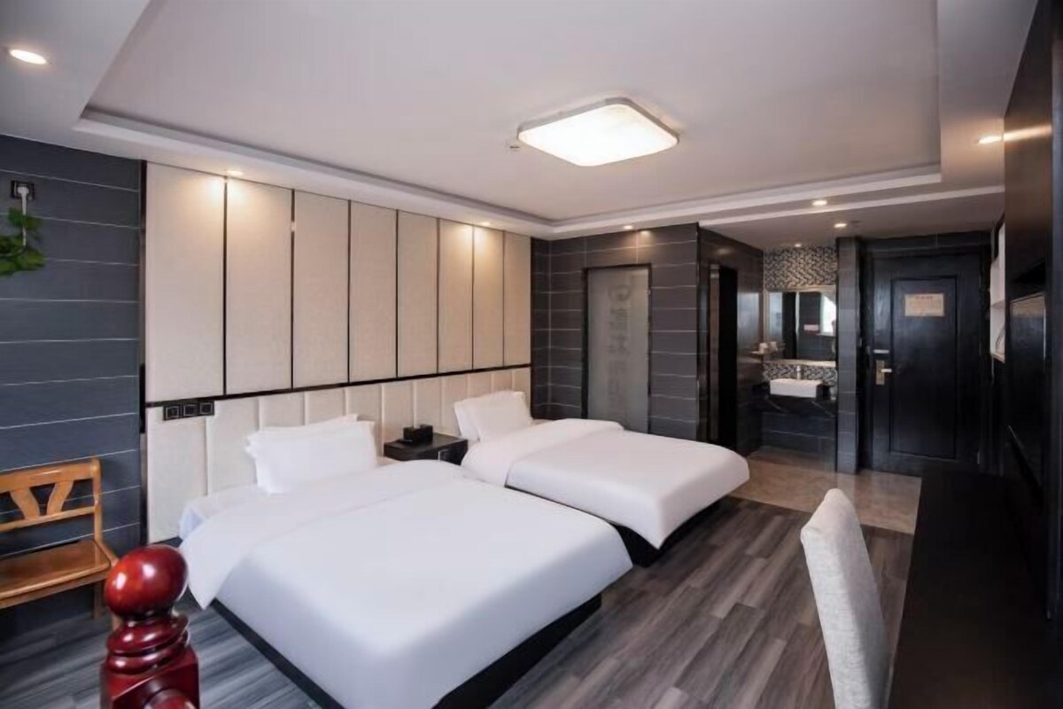 A modern hotel room with two beds, a wooden chair, a red decorative object, and a bathroom visible through an open door.