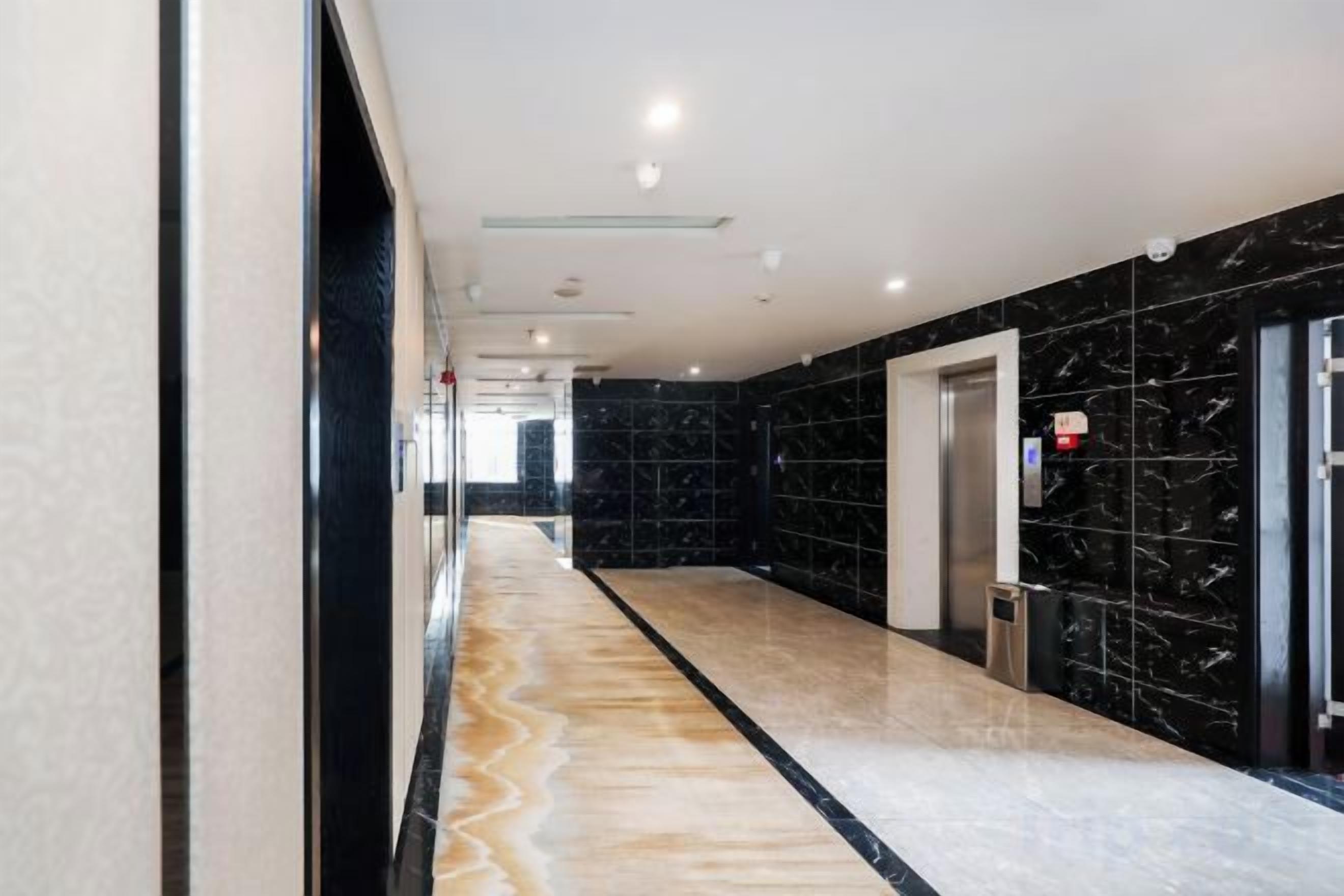 A hallway with a marble floor, a black wall with a marble pattern, and an elevator.