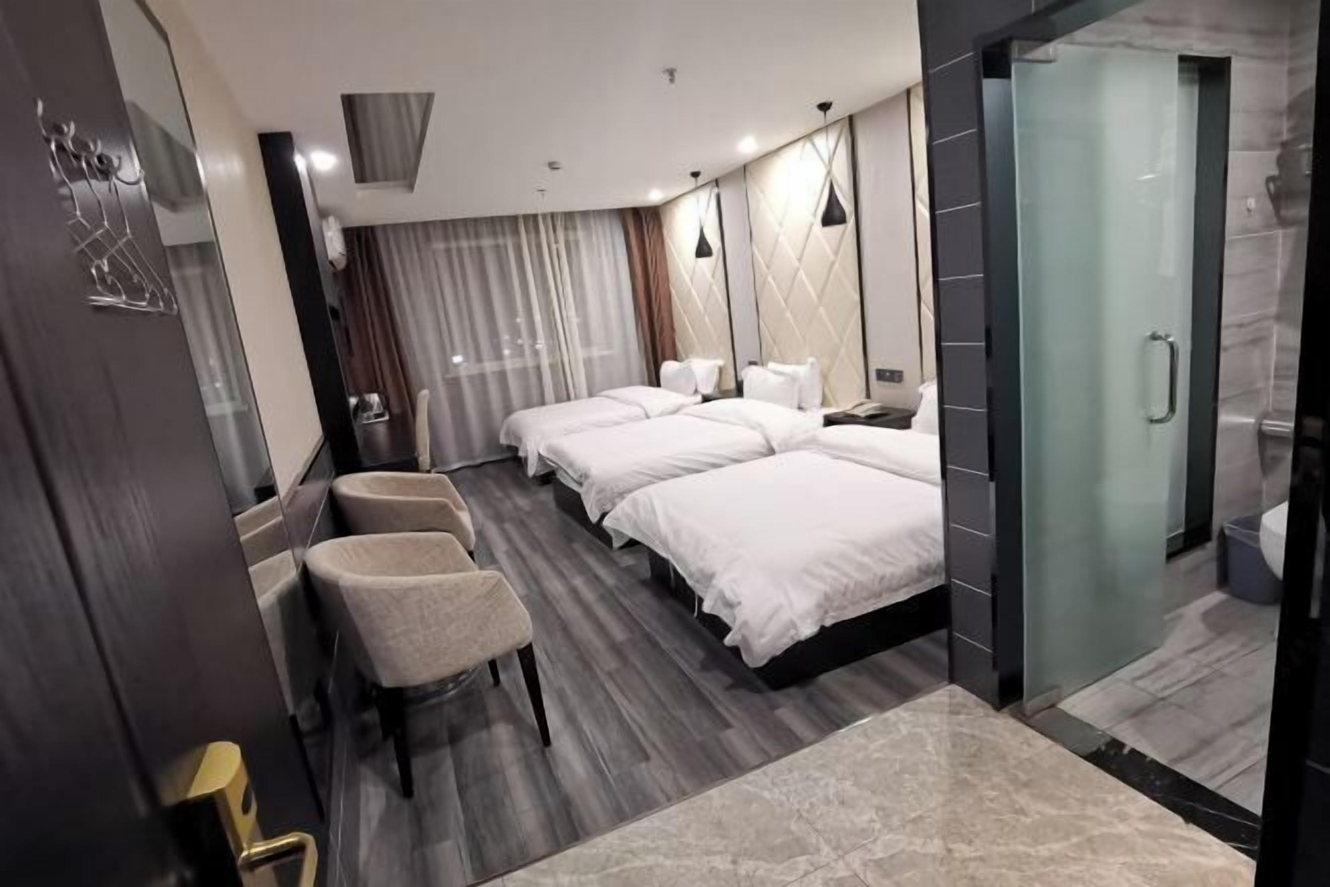 A modern hotel room with a large bed, a separate seating area, a shower, and a glass-enclosed bathroom.