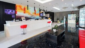 A modern hotel lobby with a reception desk, red bar stools, a black marble coffee table, and a large abstract painting on the wall. - Qingmu Hotel (Jiangyan Renmin Middle Road Branch) (Taizhou)