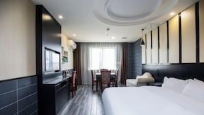A modern hotel room with a large bed, a desk with a chair, a dining table with chairs, and a large window with curtains. - Qingmu Hotel (Jiangyan Renmin Middle Road Branch) (Taizhou)