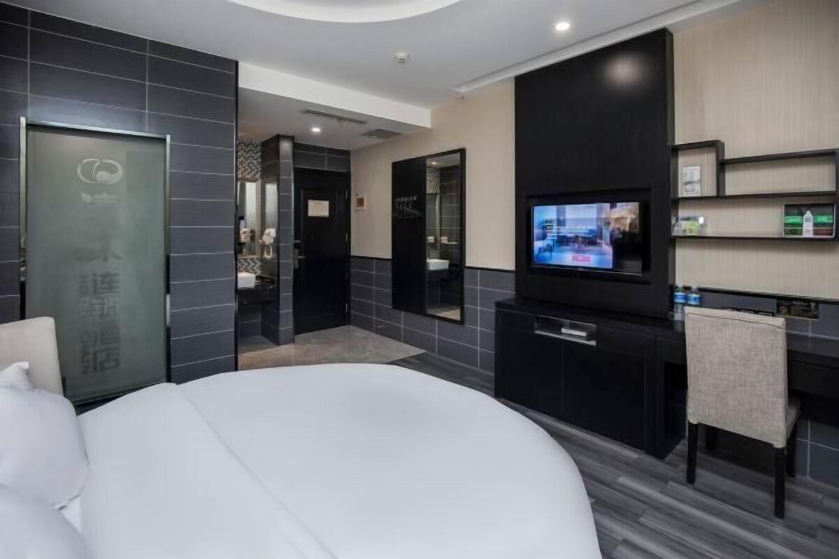 A modern hotel room with a bed, a TV, a desk, and a bathroom visible through an open door.