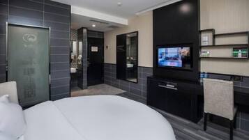 A modern hotel room with a bed, a TV, a desk, and a bathroom visible through an open door.