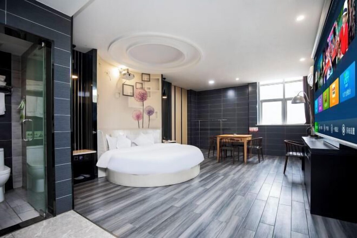 A modern hotel room with a round bed, a desk, and a television.