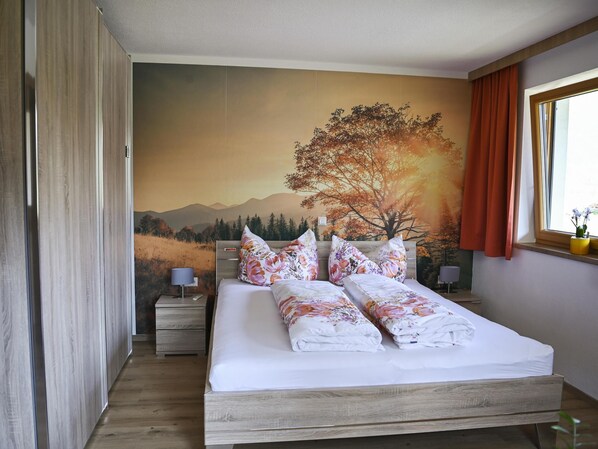 Un dormitorio con una cama grande, cabecera de madera y un mural que muestra un árbol y montañas.