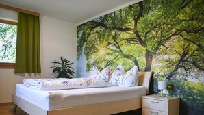 A bedroom with a bed, a nightstand, a lamp, a plant, and a large tree mural on the wall. - Apartment on the outskirts of Strass Zillertal (Strass im Zillertal)