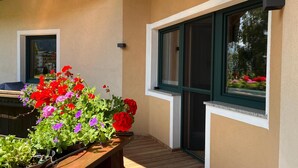 A covered outdoor area with a wooden bench, potted plants, and a window with a view of greenery. - Apartment on the outskirts of Strass Zillertal (Strass im Zillertal)